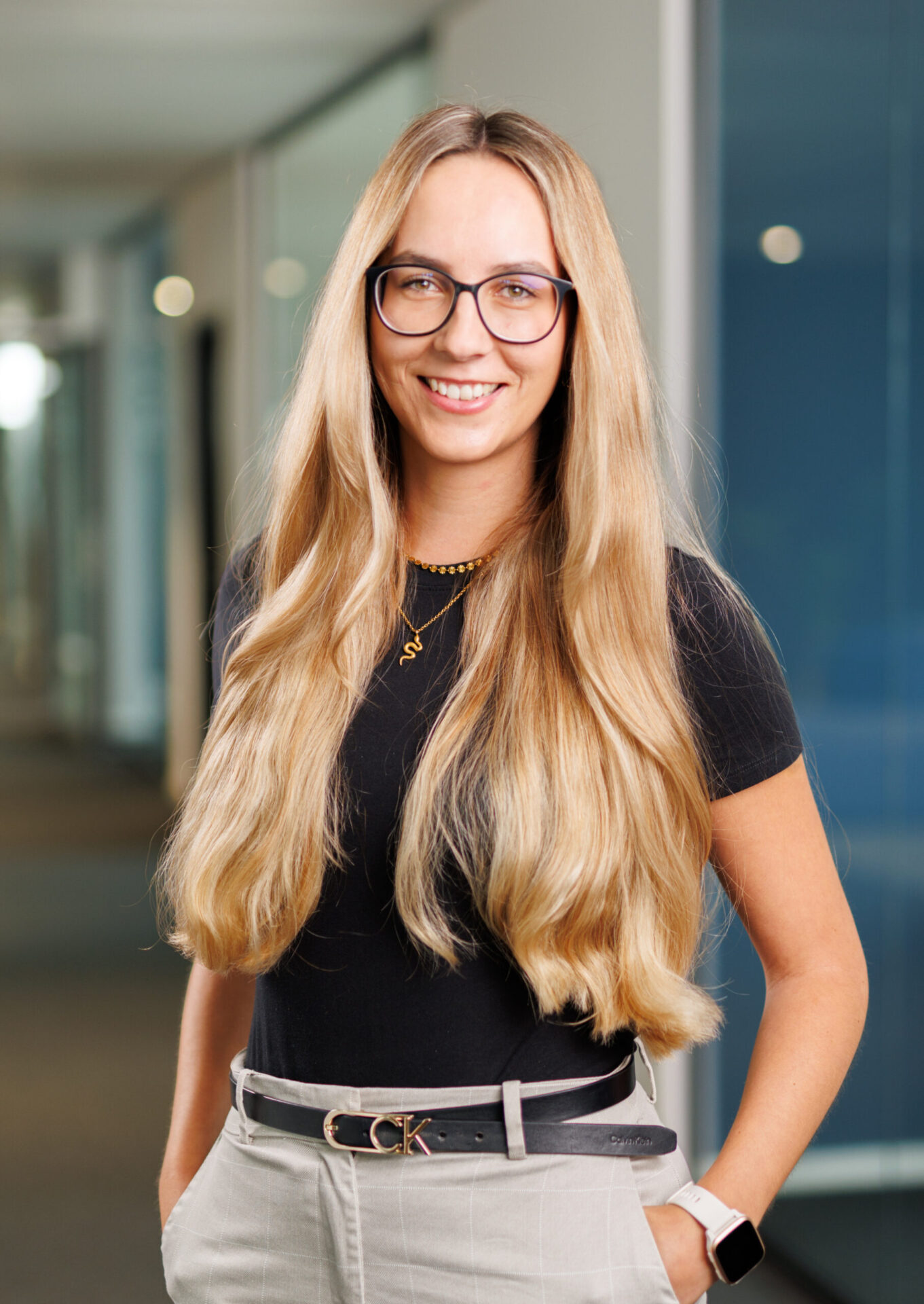 Blonde Mitarbeiterin von Makandra in schwarzem T-Shirt mit Brille vor unscharfem Bürohintergrund