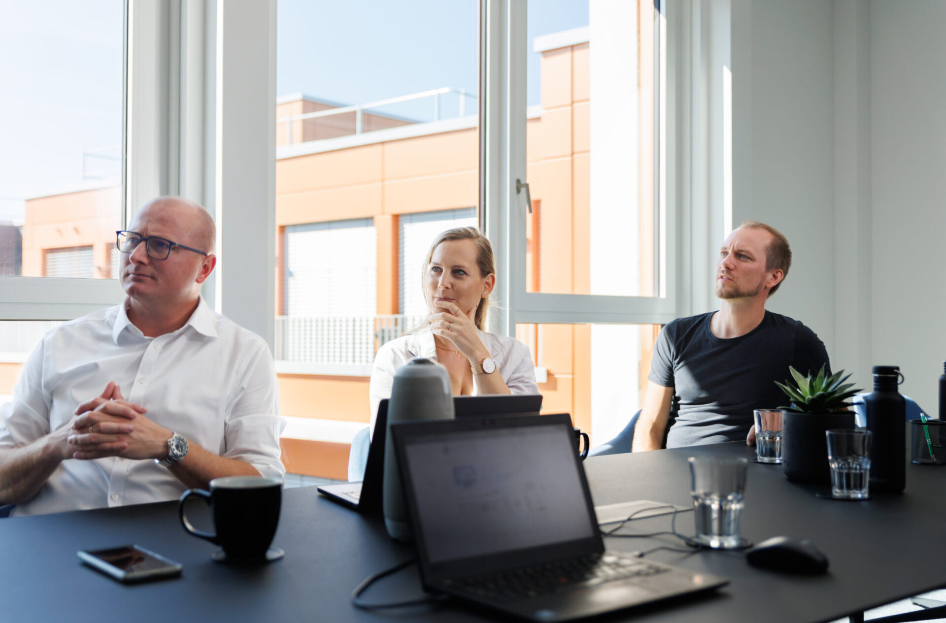 Drei Mitarbeitende sitzend in einer Reihe am Tisch blicken überlegend nach links
